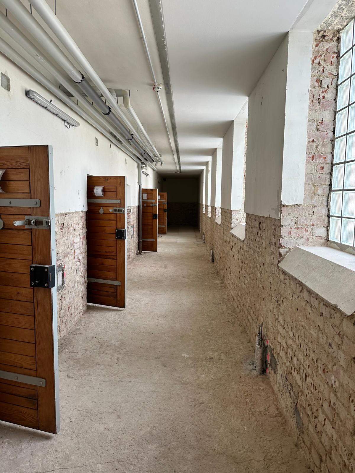Langer Flur mit Holztüren, Glasbausteinfenstern und bis in Sockelhöhe freigelegtem Ziegelmauerwerk
