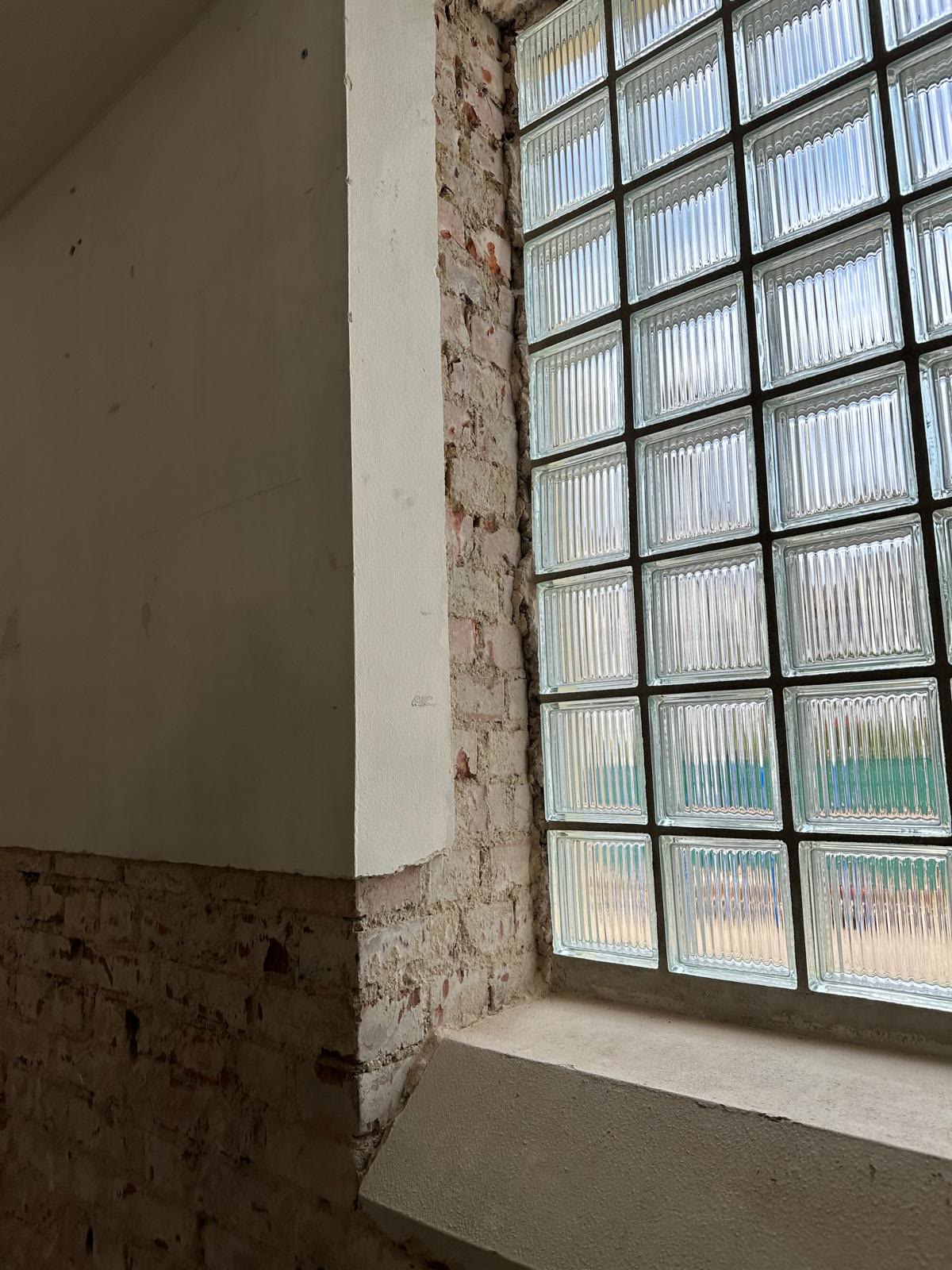 Glasbausteinfenster mit freigelegtem Ziegelmauerwerk im Sockelbereich und verputzter Wand darüber