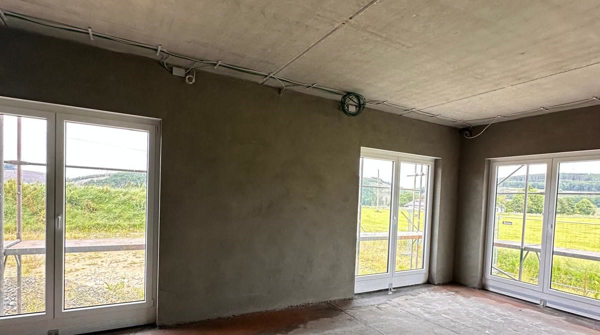 Verputzter Raum mit bodentiefen Fenstern und Blick ins Grüne